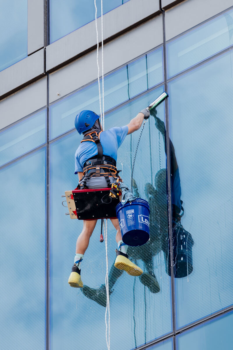 Rope access technician cleaning a glass curtain wall on a high-rise commercial building
