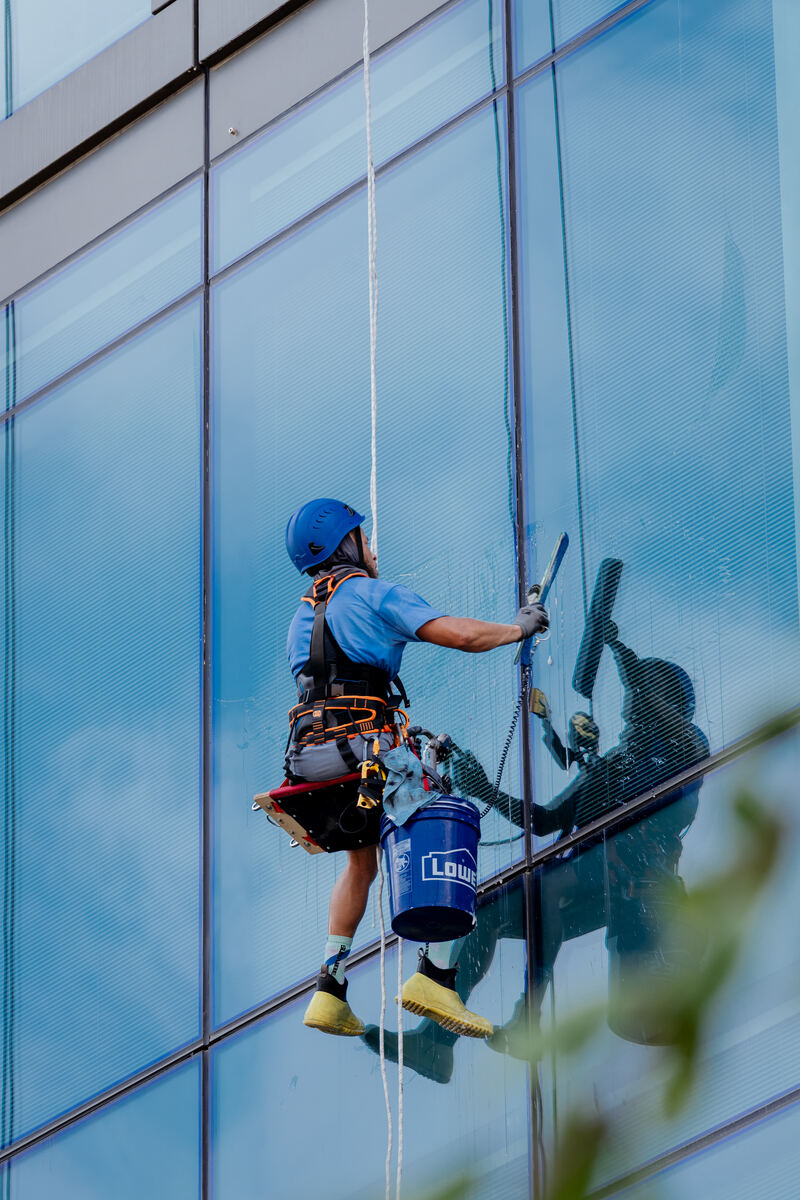Atlas Facility Services technician squeegeeing windows on a commercial tower via rope access