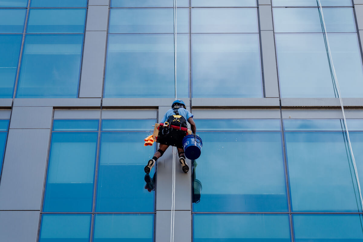 Rope access crew member with equipment harness working on a high-rise glass facade
