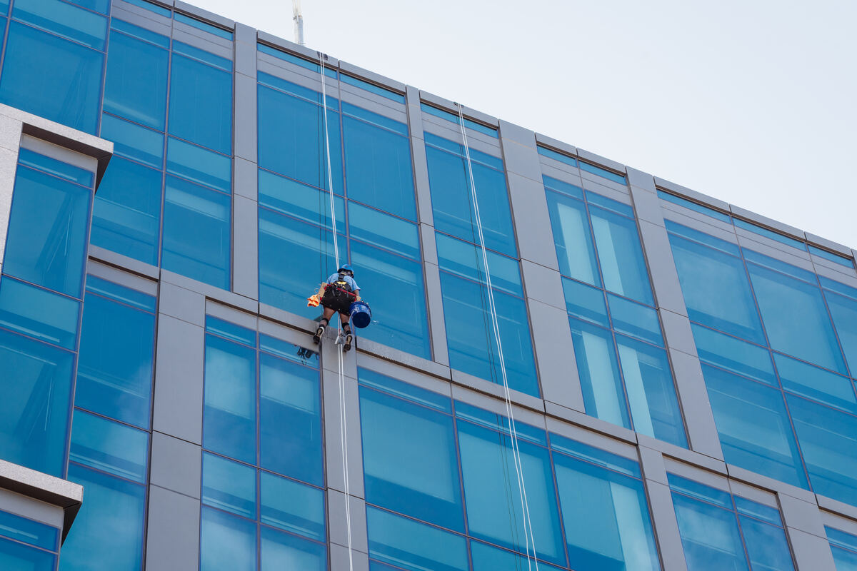 Wide view of a commercial high-rise glass tower with a rope access technician on the facade