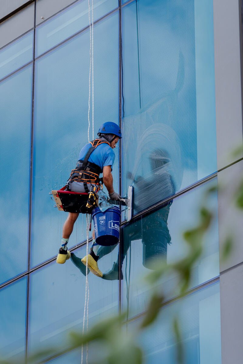 Rope access technician performing window cleaning near the building corner of a commercial high-rise